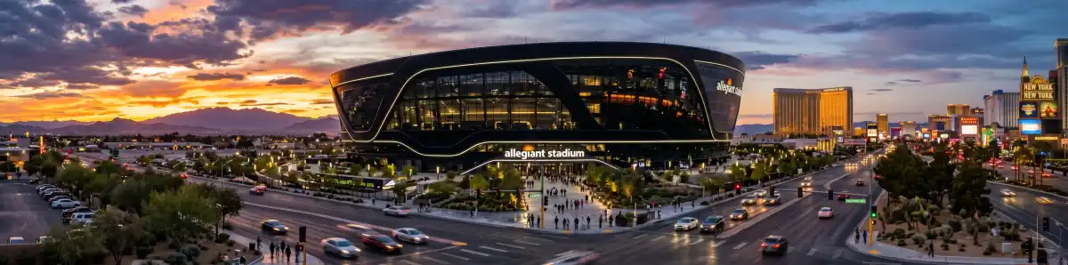 Allegiant Stadium's black translucent exterior at dusk with the Las Vegas Strip lights glowing in the background