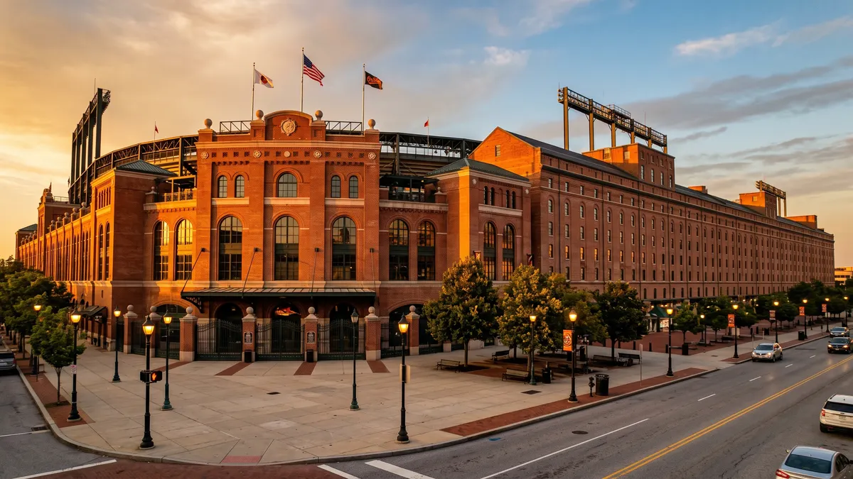 Oriole Park at Camden Yards exterior at sunset with the iconic B&O Warehouse beyond right field and fans walking along Eutaw Street
