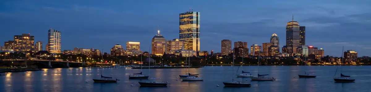 Boston Back Bay skyline at dusk with the Prudential Tower and hotel buildings illuminated along the Charles River