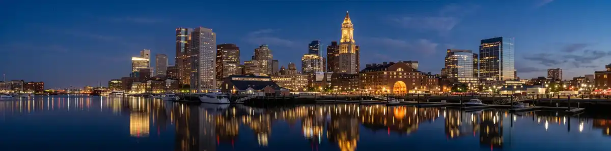 Boston waterfront skyline at night with illuminated buildings reflected in the harbor