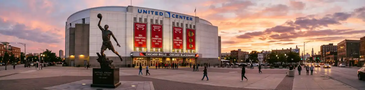 United Center exterior at dusk with the Michael Jordan statue silhouetted against arena lights, fans approaching on Madison Street